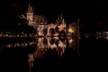 Fototapeta na wymiar Night time view of lit Vajdahunyad castle in Varosliget with reflection on the lake in Budapest Hungary