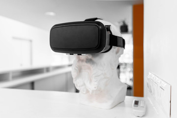 Close up of plaster bust wearing virtual reality goggles.