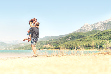 Man lifting woman in the air. Happy laughing couple on holiday. Mountain landscape. Boyfriend carrying girlfriend. Romantic moment after proposal or engagement. Passionate lovers on summer vacation.