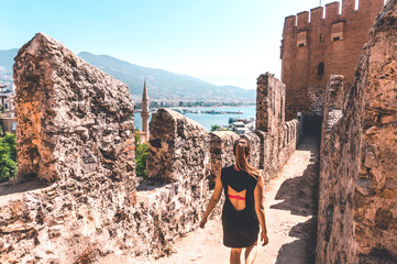 Traveler exploring the city of Alanya in Turkey. Woman walking and discovering old landmark in Europe. Tourist sightseeing in the Red Tower. Travel lifestyle, wanderlust and freedom. Summer vacation.