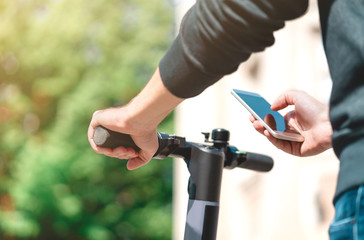 Electric scooter rent with mobile phone. Man using smartphone rental app in city street or park in...
