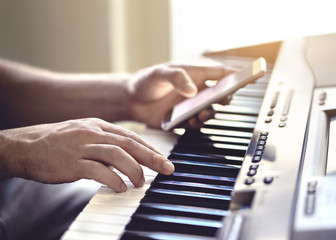 Man playing piano and using mobile phone. Person recording sound, reading notes from smartphone...