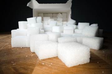 Macro shot of sugar cubes next to carton box on wooden table. Unhealthy food sweetener, sweet crystal cubes