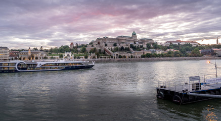 Fototapeta na wymiar Buda castle with a river cruise passing by on the Danube with dramatic sunset sky in Budapest Hungary