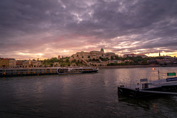 Buda castle with a river cruise passing by on the Danube with dramatic sunset sky