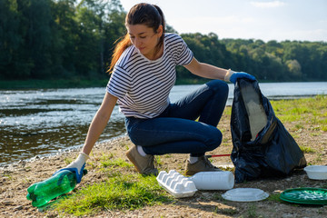 Volunteer woman collecting plastic rubbish on coast of the river. Cleaning environment concept