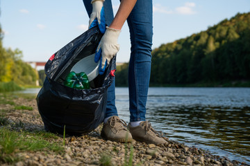 Volunteer woman collecting plastic rubbish on coast of the river. Cleaning environment concept