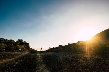 active teenager doing jogging and running alone in mountain to be fitness guy - man in distance doing sport with sunset