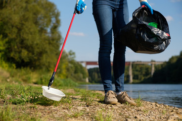 Volunteer woman picking up plastic litter on coast of the river. Cleaning environment concept