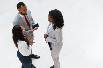 Business colleagues meeting and chatting in office hallway. Business man and women standing in circle, holding tablet and papers, talking and laughing. Work break concept