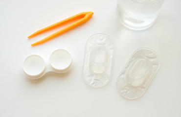 Accessories for use of contact lenses: case, tweezers, blister pack and solution on white background. Safe vision correction. View from above.
