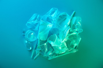 top view of pile of crumpled plastic bags, cups, straws and forks with copy space in blue light