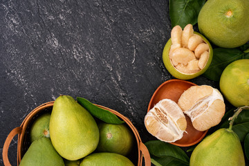 Fresh pomelo, pummelo, grapefruit, shaddock in bamboo basket with leaf on dark black slate...