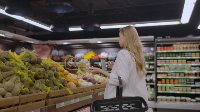 At the Supermarket: Beautiful Young Woman Walks Through Fresh Produce Section, Chooses Vegetables and Puts them in Her Shopping Cart.