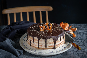 Beautifully styled and decorated birthday cake with no candle, on a table with chair in the background, oranges, walnut and chocolate decoration, dark, moody background with negative space for title a