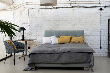 Bedroom interior with double bed in grey color and white wall with copy space. Loft apartment.