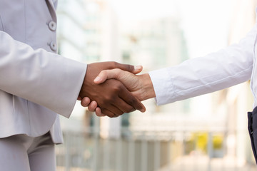 Female business colleagues shaking hands. Diverse business women in formal clothing meeting outside. Handshake closeup concept
