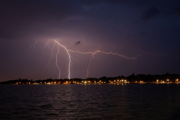 Naklejka na ściany i meble Lightning over a little town on a coast of a lake at night.
