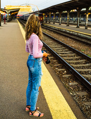 Young girl walking alone on train platform and taking photos on railway station