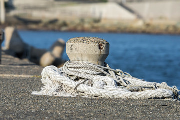 Fototapeta premium Concrete mooring bollard with a rope around it at a dock. 