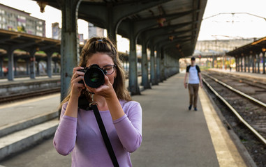 Young girl walking alone on train platform and taking photos on railway station