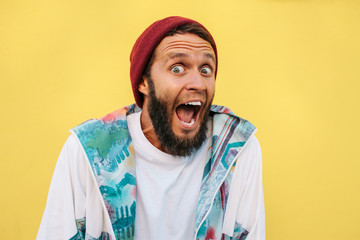 Stylish young hipster man with beard in red hat and a retro jacket of 90s on yellow background....