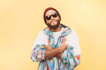 Stylish young hipster man with beard in red hat and a retro jacket of 90s on yellow...