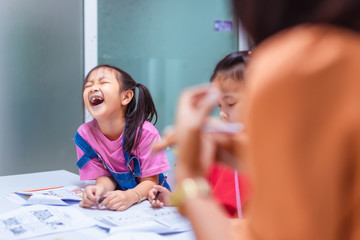 Asian elementary school children wearing red and pink T-shirts are studying in the classroom with an Asian woman teacher.