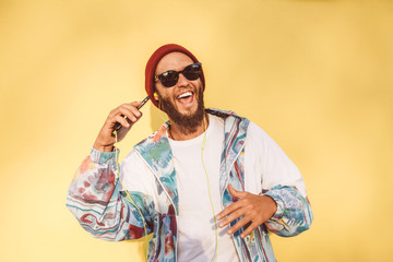 Stylish young hipster man with beard in red hat and a retro jacket of 90s on yellow background...