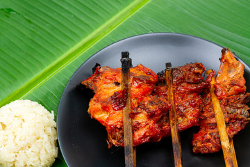 Grilled chicken with sticky rice or Gai Yang on black plate ceramic, very delicious local Thai food on fresh banana green leaf. Street food in Thailand.