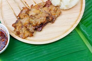 Grilled pork with sticky rice or Khao Niew Moo Yang on wooden plate and spicy sauce , local Thai food on fresh banana green leaf.