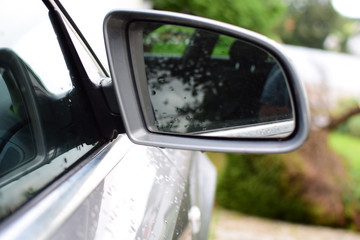 Obraz premium Fragment of a silver car with a side mirror. Raindrops on the mirror.