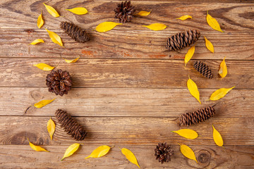 Pine cones and small yellow leaves on wooden background. Top view. Copy space.