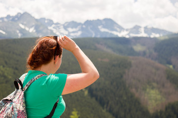 Fototapeta na wymiar Woman traveler with backpack looking at amazing mountains and forest, wanderlust travel concept, space for text, atmospheric epic moment