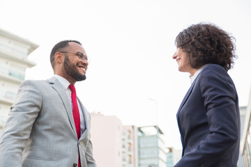 Multiethnic business people smiling each other. Low angle view of cheerful businessman and businesswoman looking at each other on street. Cooperation concept