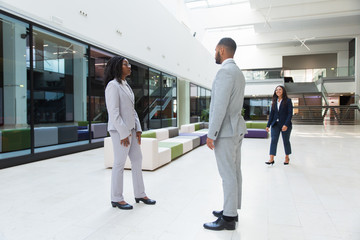 Three diverse colleagues meeting in office hall. Business man and women standing or walking in hallway, talking, smiling. Corporate relationship concept