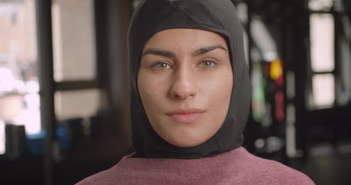 Closeup portrait of young attractive athletic muslim female in hijab looking at camera in gym indoors