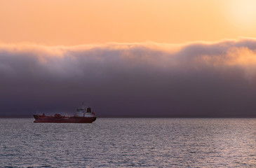 Heavy vessel on the horizon under dramatic clouds and bright sky. Beautiful African sunset. 