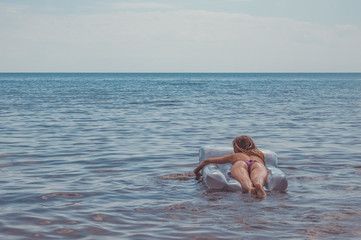 Fascinating a young girl in a swimsuit swimming in the sea. Adorable girl swims with air mattress...