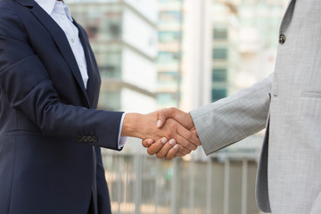 Partners greeting each other in business district. Business man and woman in office suits shaking hands outside. Handshake closeup concept