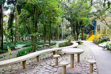 Trail paved with stones, a cement bank and table. Green trees and a playground