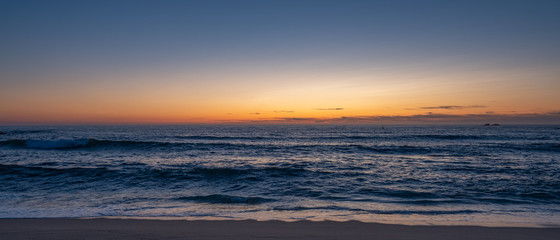 Fototapeta na wymiar Wide shot over beach at dusk, parallel to shoreline with blue orange gradient sky