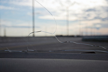 Cracks on car windshield glass hit by stone ejected from under the wheels of another car. View from...