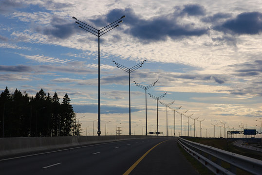 Nightfall view of empty highway against evening sky, row of light pillars, road safety barrier, asphalt road goin into the distance