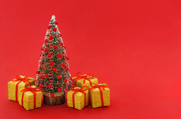 Decorative Christmas tree with red balls and small gold gift boxes near on red background, with empty place for text on the right. . New Year and Christmas holiday celebration concept.