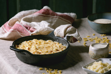 Classic american dish baked mac and cheese in cast iron pan with kitchen towel and ingredients above on kitchen table with linen tablecloth. Dark rustik style