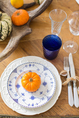 Luxurious elegant wedding decor in autumn style. Wooden vintage table setting with ceramic plates and silver cutlery. Fresh flowers in a vase, orange pumpkins, deer horns and candles. Romantic dinner.