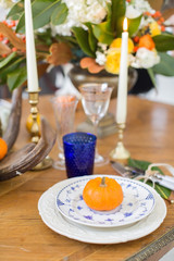 Luxurious elegant wedding decor in autumn style. Wooden vintage table setting with ceramic plates and silver cutlery. Fresh flowers in a vase, orange pumpkins, deer horns and candles. Romantic dinner.