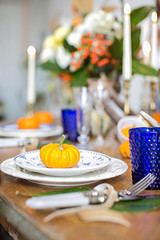 Luxurious elegant wedding decor in autumn style. Wooden vintage table setting with ceramic plates and silver cutlery. Fresh flowers in a vase, orange pumpkins, deer horns and candles. Romantic dinner.