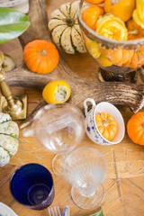 Luxurious elegant wedding decor in autumn style. Wooden vintage table setting with ceramic plates and silver cutlery. Fresh flowers in a vase, orange pumpkins, deer horns and candles. Romantic dinner.